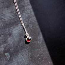 Load image into Gallery viewer, Silver necklace with a red gemstone pendant on a textured black surface
