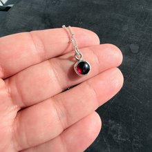 Load image into Gallery viewer, Silver necklace with a pendant featuring red and black gemstones held in a hand against a dark background.
