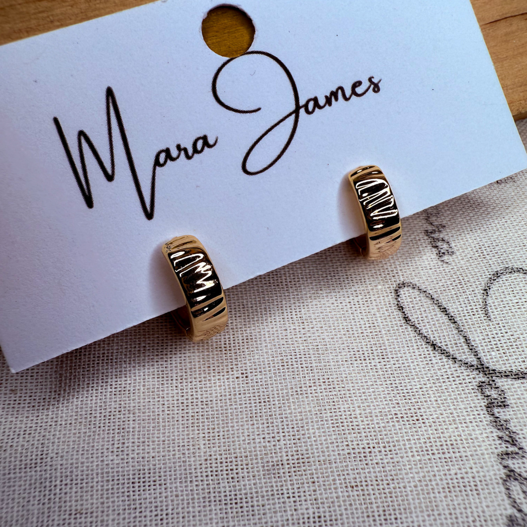 A pair of gold-plated textured huggie earrings displayed on a card with the brand name 'Mara James'.