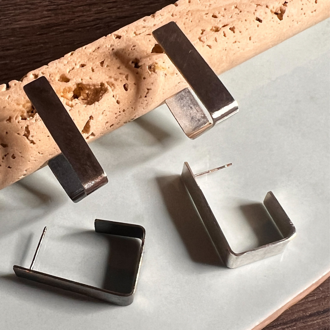 This image features a pair of elegant Angular Hoop Earrings crafted from sterling silver. The earrings exhibit a sleek, contemporary design with a polished finish, contrasting beautifully against the textured surface of a freshly baked loaf.