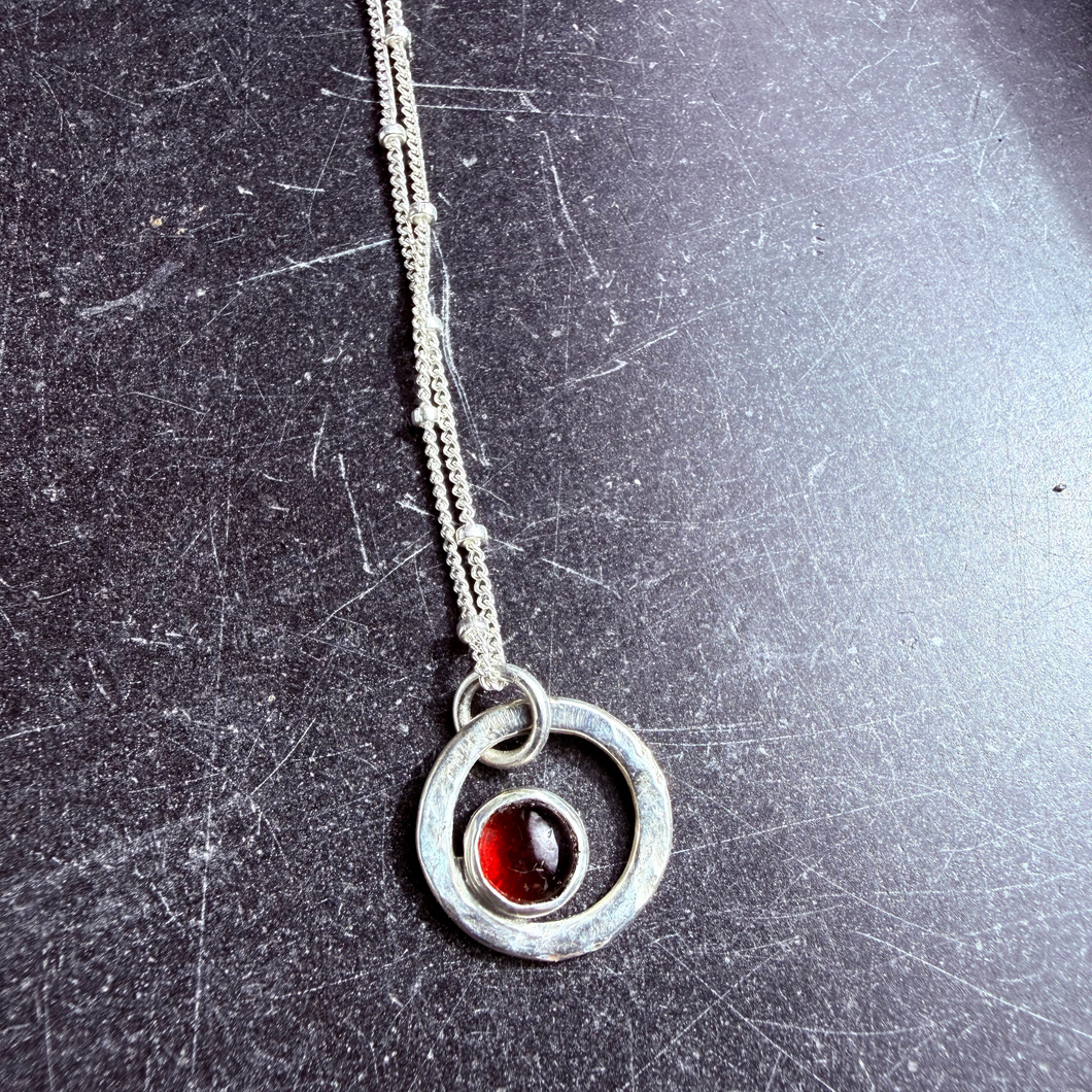 Handcrafted sterling-silver necklace featuring a round garnet gemstone set in a hammered silver circle.