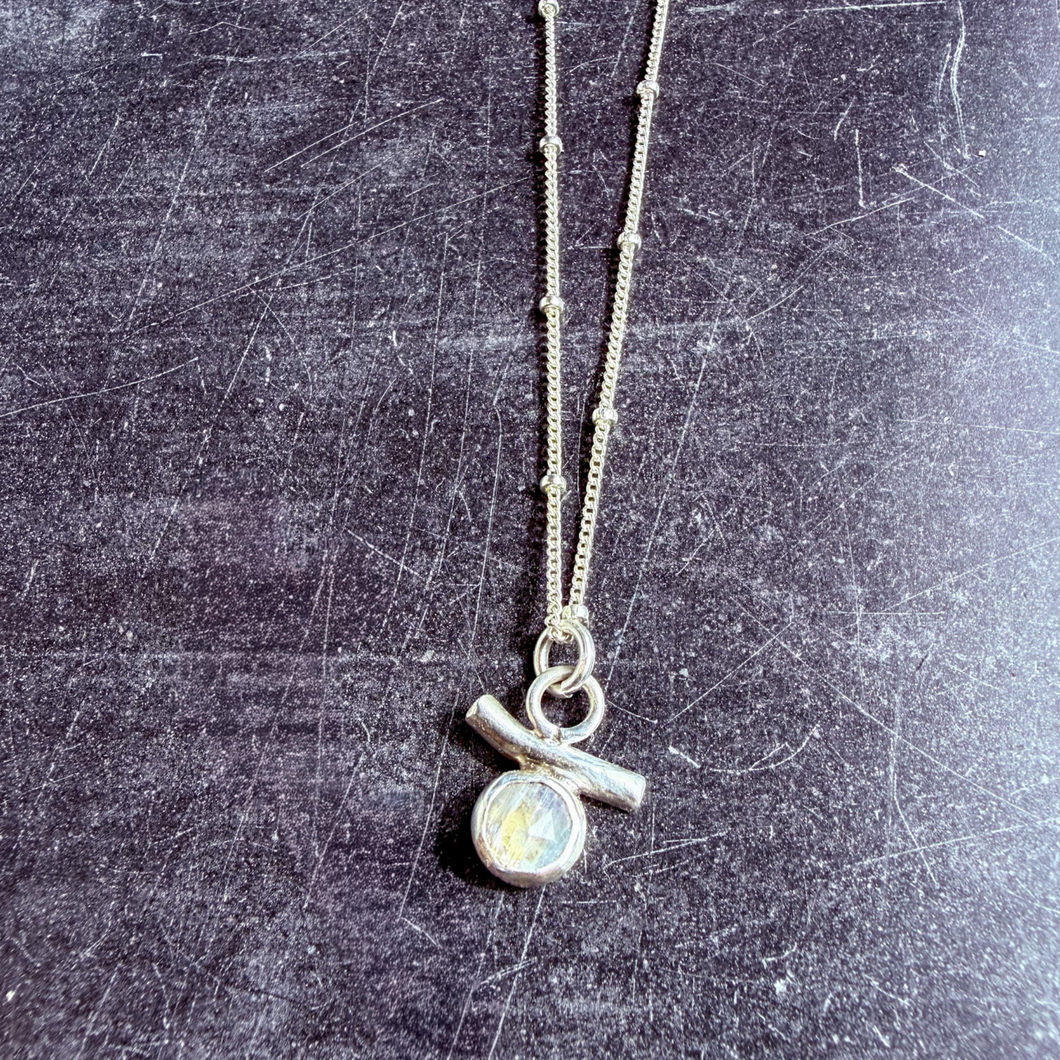 Handcrafted sterling silver earrings featuring faceted rainbow moonstones set above curved silver bars, photographed on a dark textured background.
