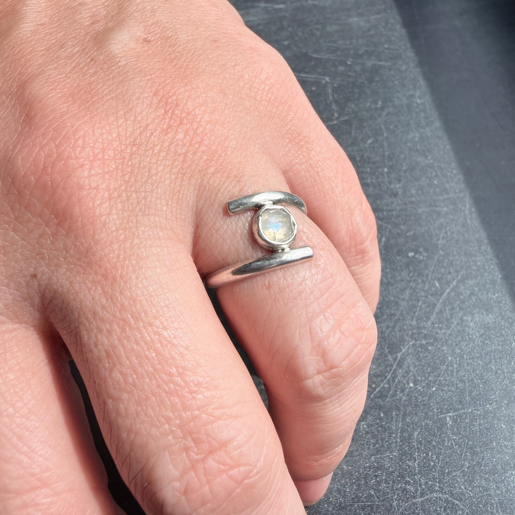 Handcrafted sterling silver ring featuring a luminous rainbow moonstone set between two horizontal silver bars, worn on hand in natural sunlight.