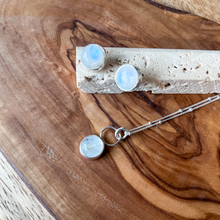 Load image into Gallery viewer, A pair of sterling silver earrings with moonstone studs placed on a wooden surface.
