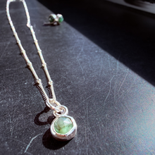 Load image into Gallery viewer, Necklace with a green pendant on a dark surface
