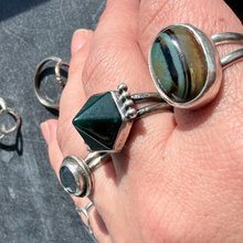 Load image into Gallery viewer, Close-up of a hand wearing multiple silver rings with gemstones on a dark surface.
