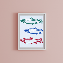 Load image into Gallery viewer, Framed artwork with three stylized fish illustrations on a white background, framed in gray against a pink wall.
