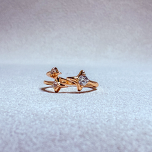 Load image into Gallery viewer, A pair of rose gold rings with star-shaped settings and clear gemstones, displayed on a textured light gray surface.

